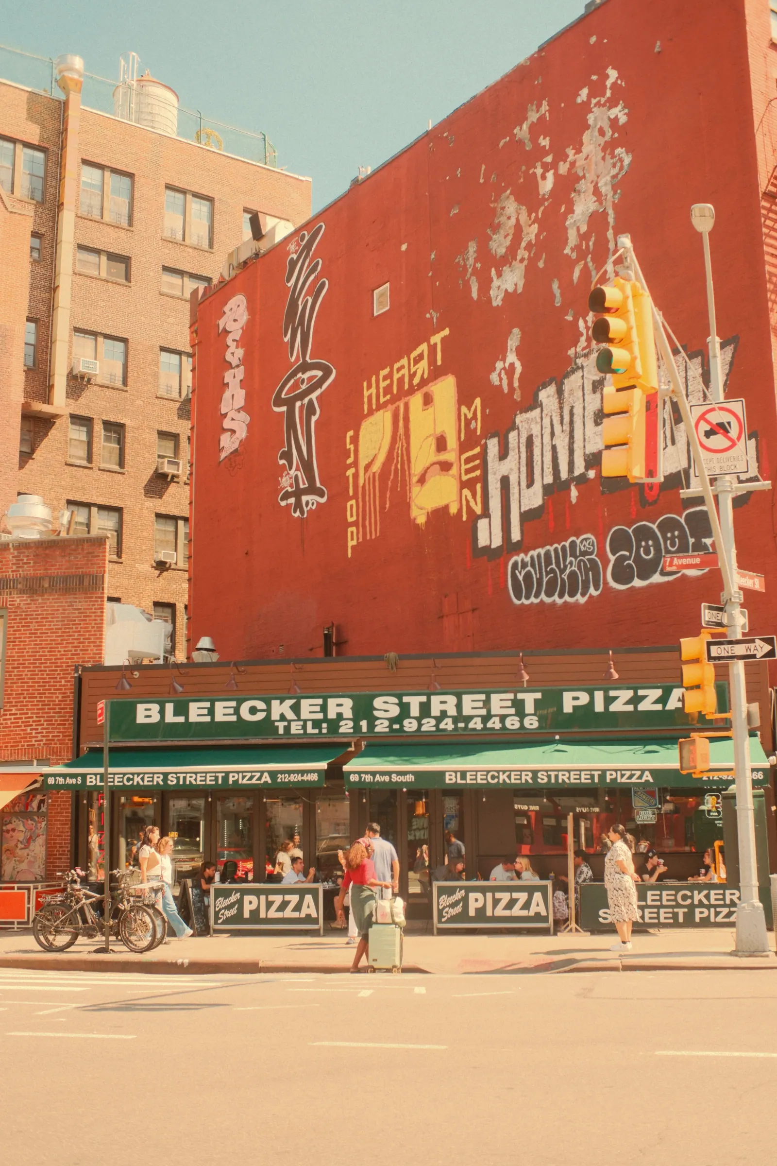 Bleecker Street Pizza beneath a red mural on a sunny Greenwich Village corner.
