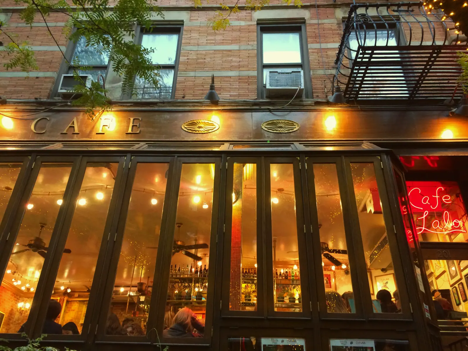 An illuminated Café Lalo storefront beneath Upper West Side windows and a fire escape.